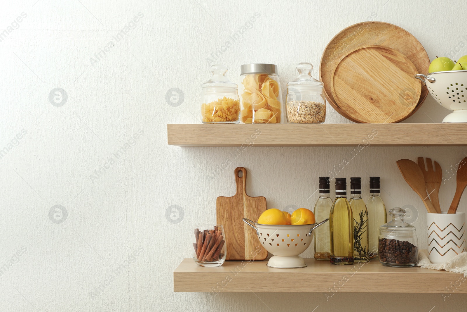 Photo of Wooden shelves with dishware and products on white wall. Kitchen interior idea