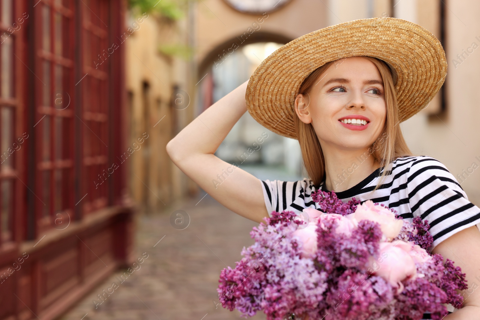 Photo of Beautiful woman with bouquet of spring flowers on city street, space for text