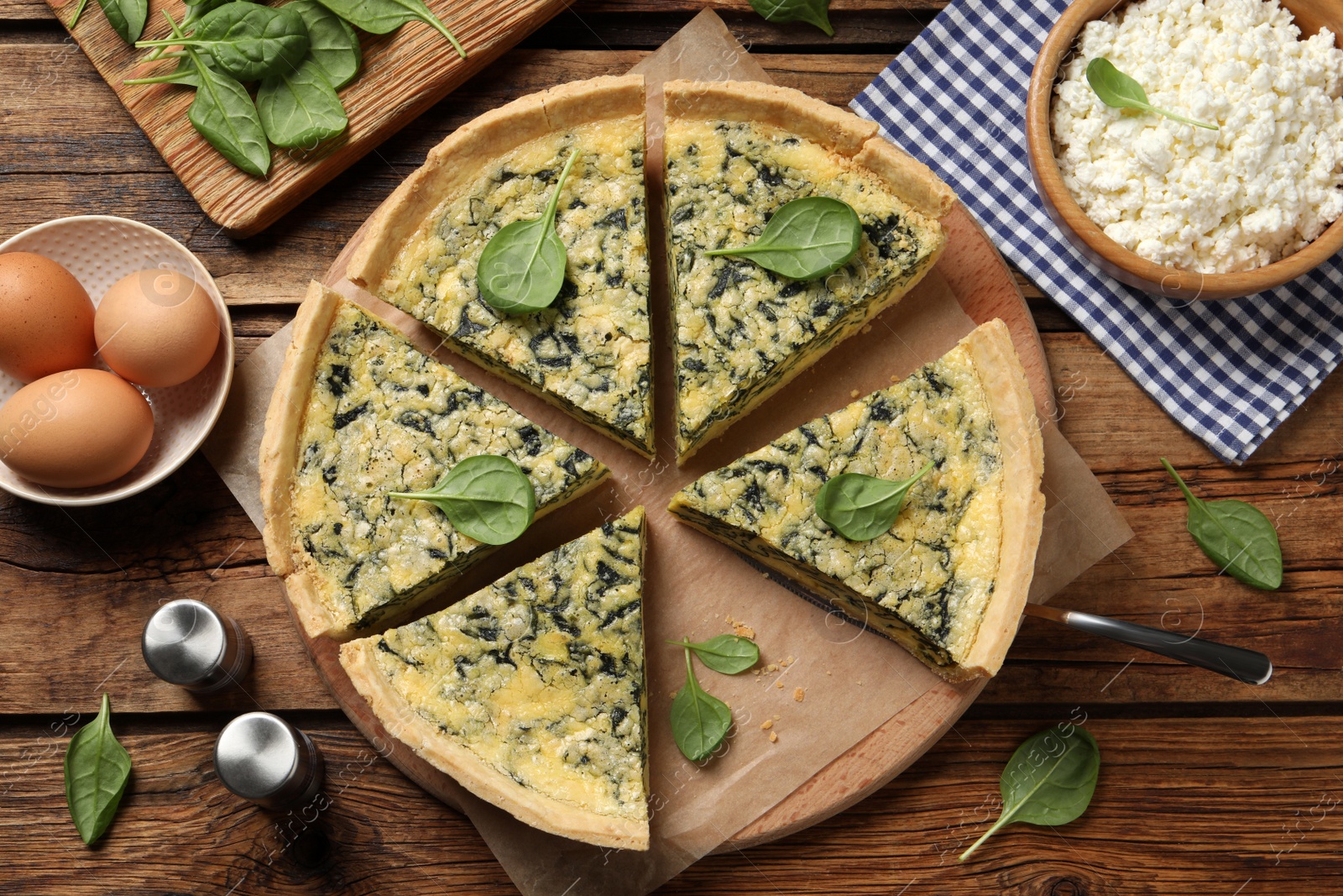 Photo of Cut delicious spinach pie with ingredients on wooden table, flat lay