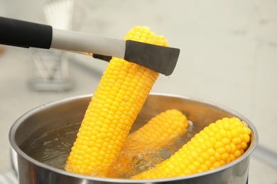 Photo of Taking boiled corn from pot with tongs in kitchen, closeup