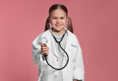 Little girl in medical uniform with stethoscope on pink background