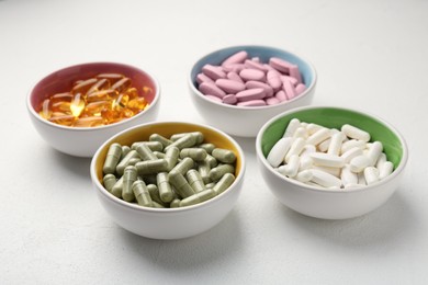 Different vitamin capsules in bowls on white wooden table