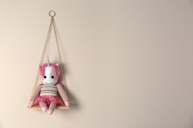 Photo of Shelf with cute toy unicorn on beige wall, space for text. Child's room interior element
