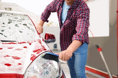 Young man cleaning vehicle with brush at self-service car wash