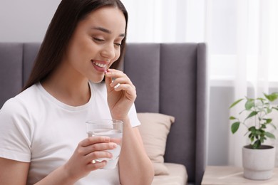 Photo of Beautiful woman with glass of water taking pill at home, space for text