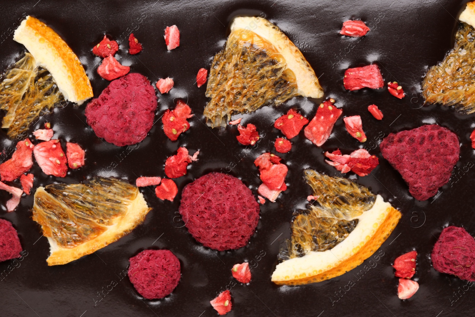 Photo of Chocolate bar with freeze dried oranges and berries as background, closeup