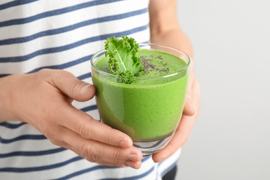 Woman holding tasty kale smoothie with chia seeds on light background, closeup