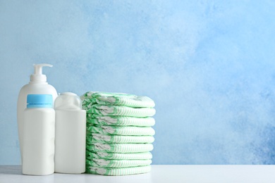 Photo of Stack of diapers and toiletries on table against color background, space for text. Baby accessories