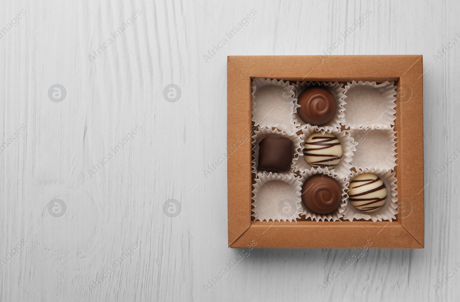 Photo of Partially empty box of chocolate candies on white wooden table, top view. Space for text