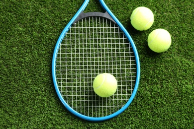 Photo of Tennis racket and balls on green grass, flat lay. Sports equipment