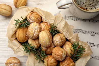 Photo of Homemade walnut shaped cookies with powdered sugar and fir branches in box on white wooden table, flat lay