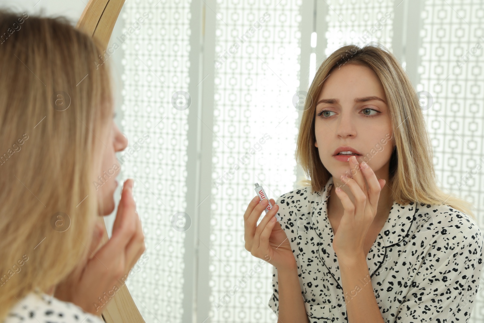 Photo of Woman with herpes applying cream onto lip near mirror at home