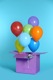 Gift box with bright air balloons on color background