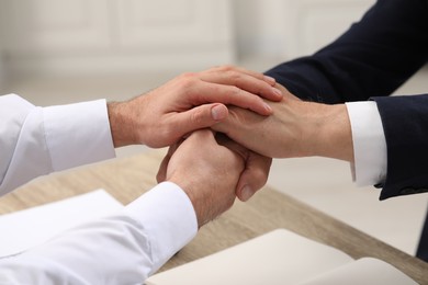 Trust and deal. Men joining hands at table indoors, closeup