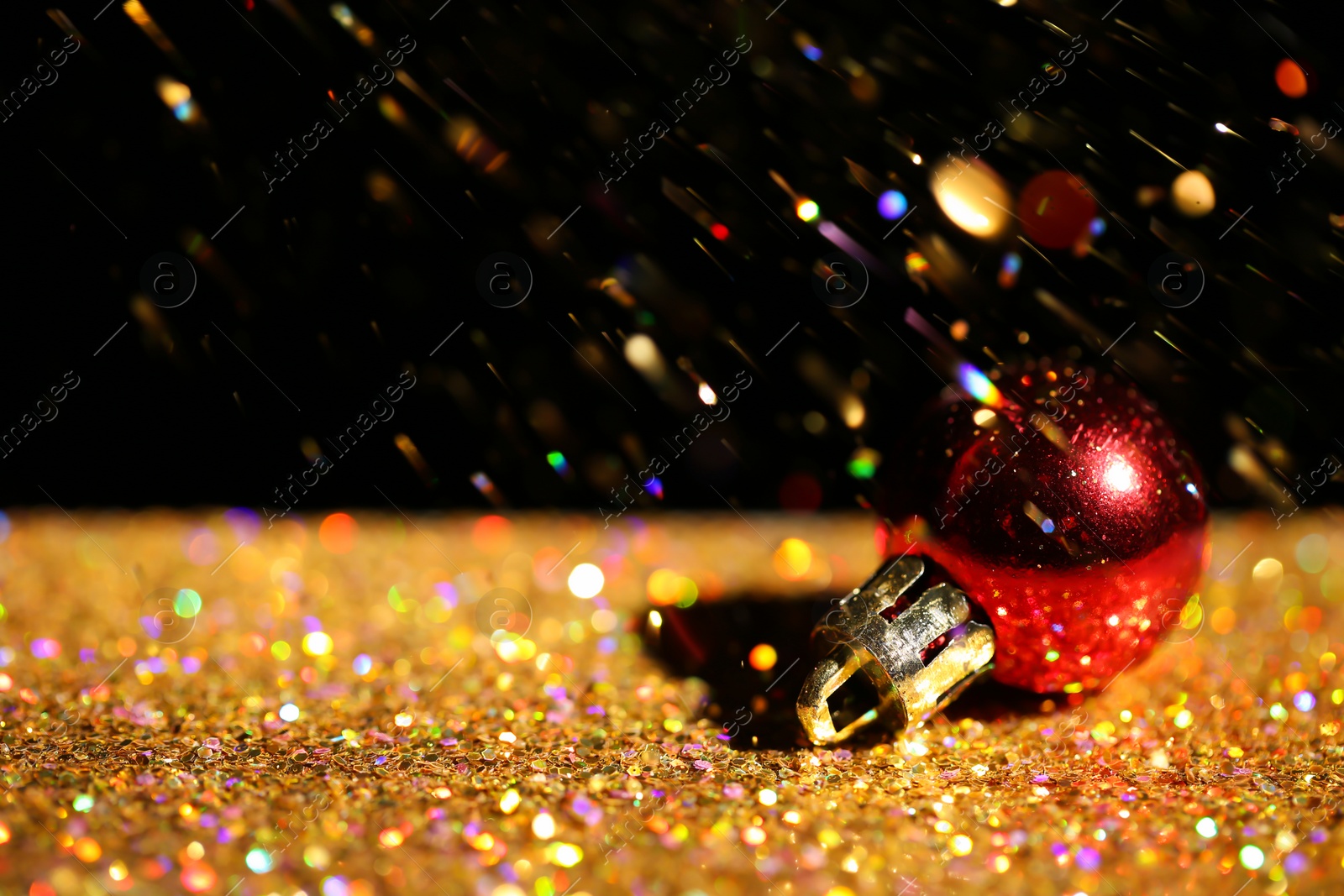 Photo of Golden paillettes and Christmas ball against black background. Space for text