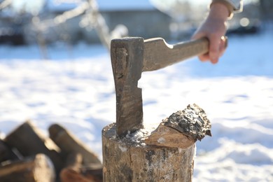Photo of Man taking axe out of wooden log outdoors on sunny day, closeup