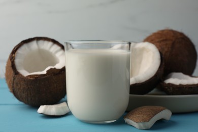 Glass of delicious vegan milk and coconuts on light blue wooden table