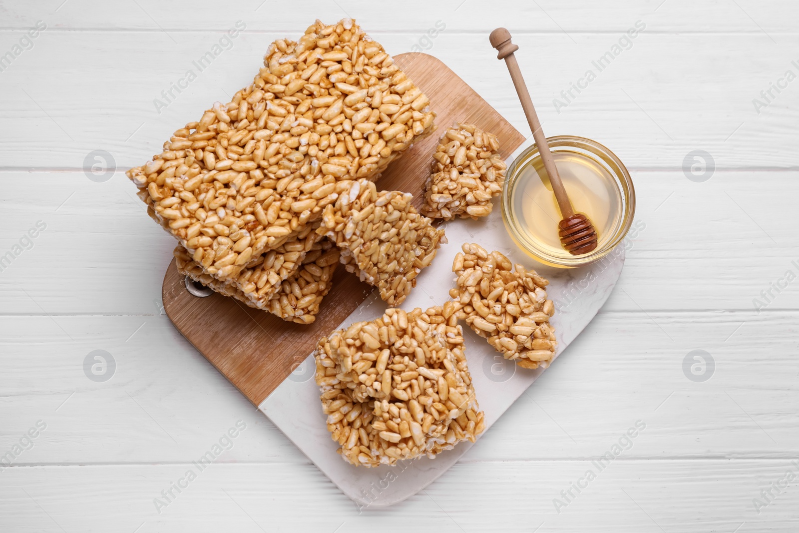 Photo of Puffed rice bars (kozinaki) and honey on white wooden table, top view