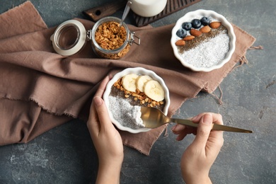 Young woman eating tasty chia seed pudding with banana and granola at table, top view