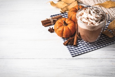 Photo of Delicious pumpkin latte and ingredients on white wooden table. Space for text