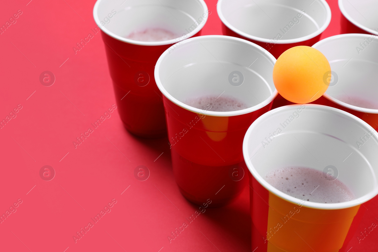 Photo of Plastic cups and ball on red background, space for text. Beer pong game