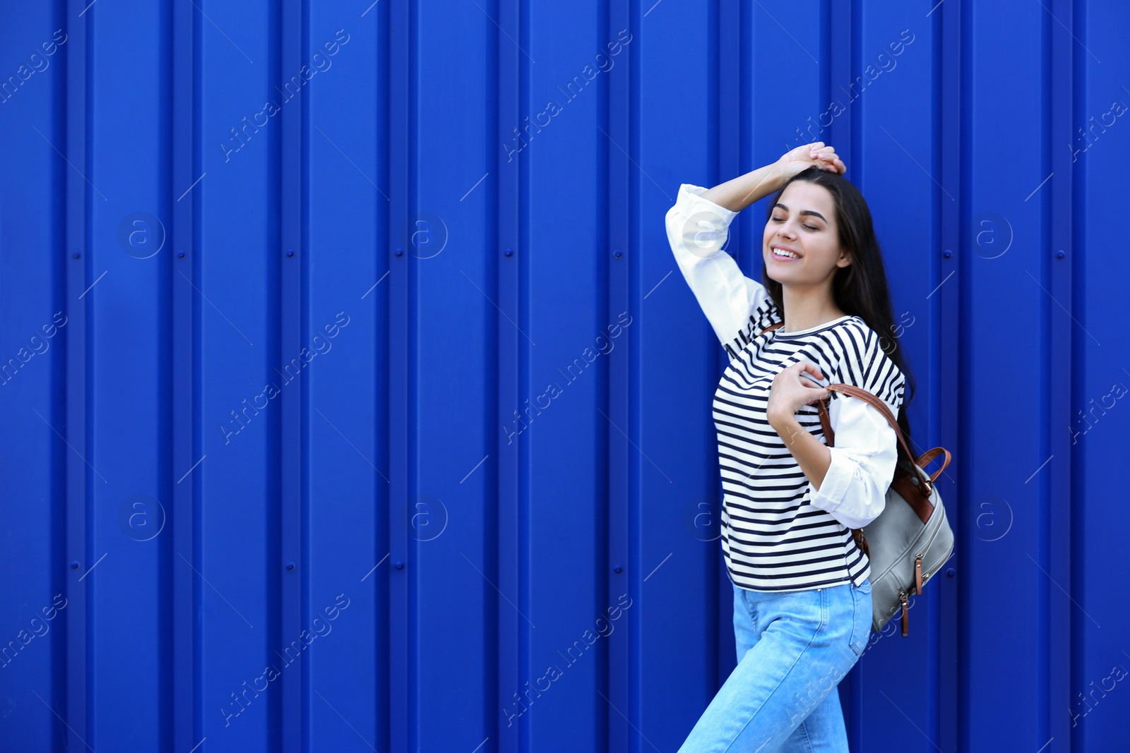 Photo of Young hipster woman in stylish jeans posing near color wall