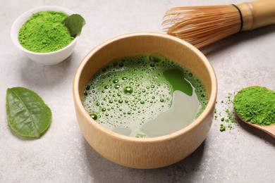 Photo of Bowl of fresh matcha tea, bamboo whisk and powder on light table