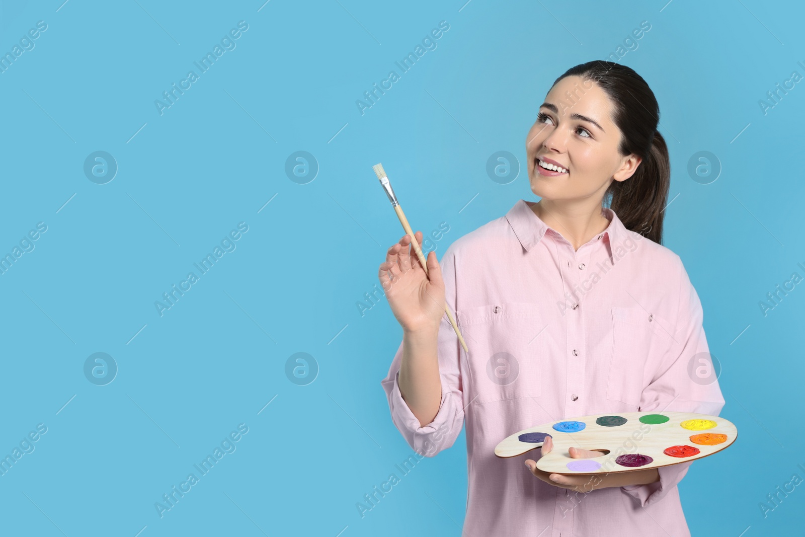 Photo of Woman with painting tools on light blue background, space for text. Young artist