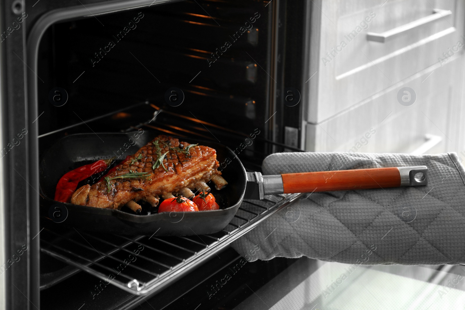 Photo of Chef taking pan with delicious roasted ribs out of oven, closeup