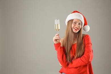 Photo of Young beautiful woman in Santa hat with glass of champagne on grey background. Christmas celebration