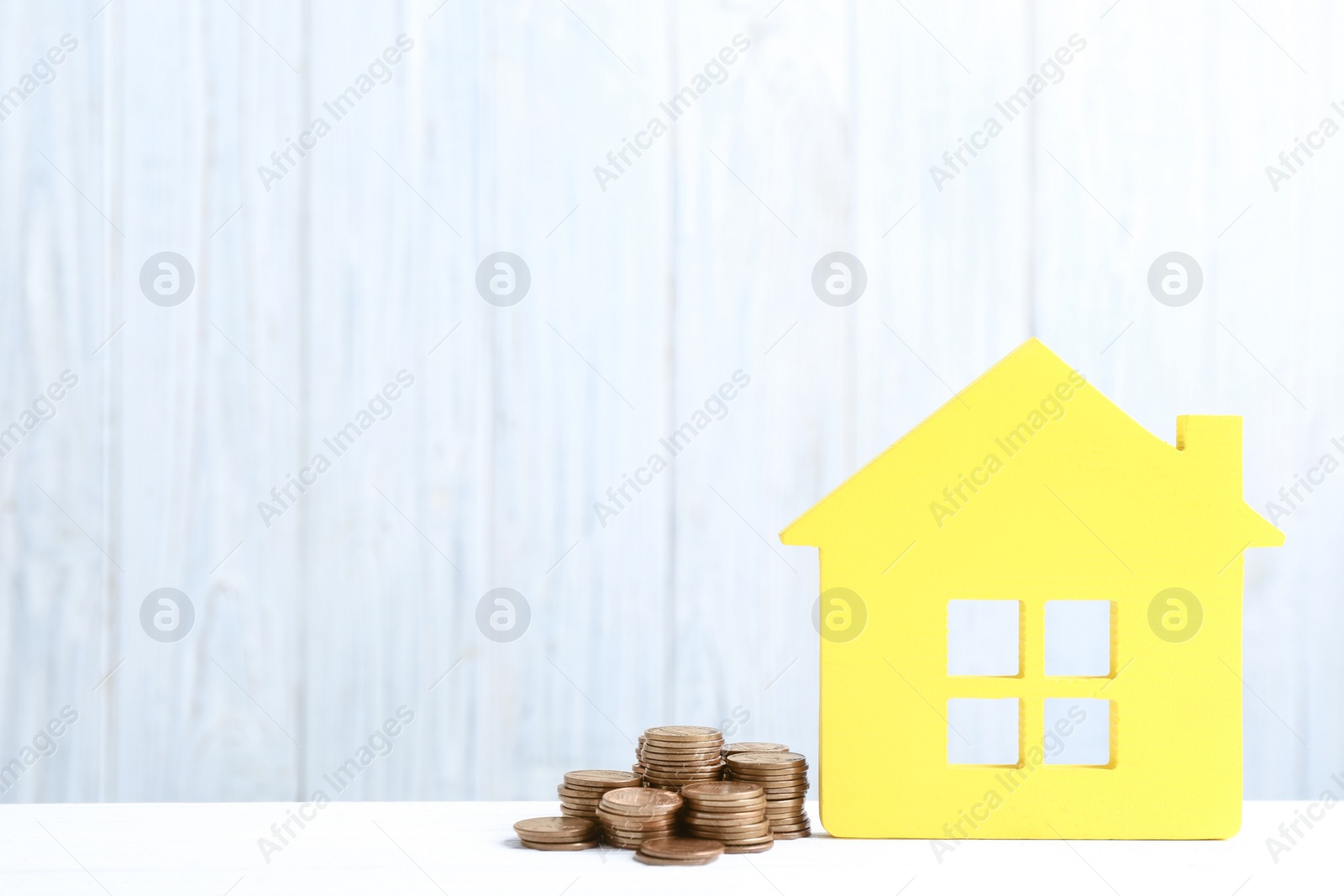 Photo of House model and coins on table against wooden background. Space for text