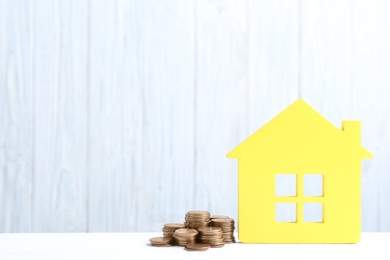 Photo of House model and coins on table against wooden background. Space for text