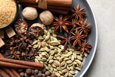 Plate with different aromatic spices on light textured table, top view