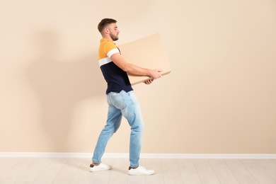 Full length portrait of young man carrying carton box near color wall. Posture concept