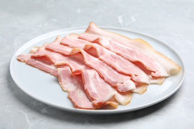 Photo of Plate of sliced raw bacon on light grey marble table