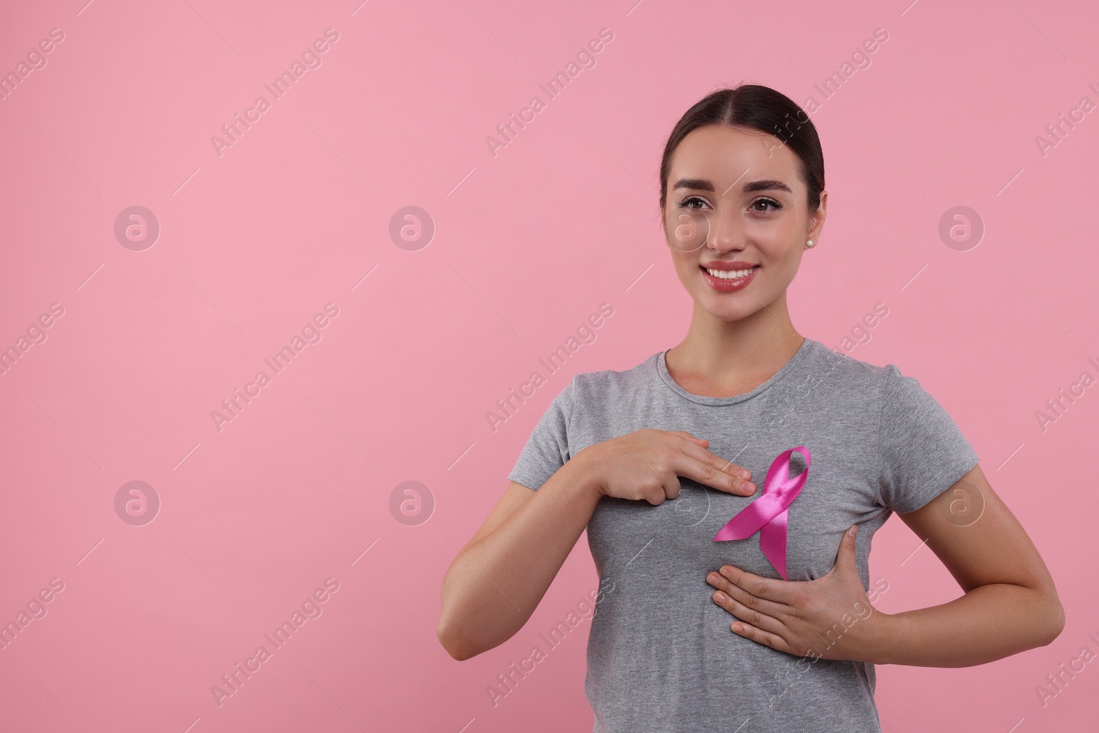 Photo of Beautiful young woman with pink ribbon on color background, space for text. Breast cancer awareness