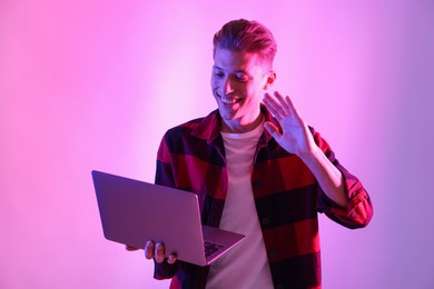 Photo of Young man with laptop talking via video chat on pink background in neon lights