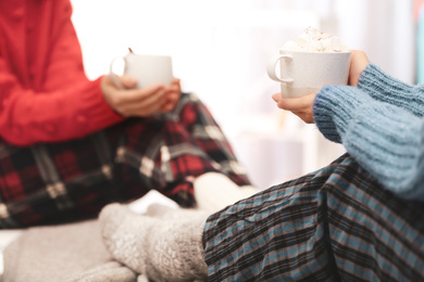 Photo of Women holding cups of hot cocoa with marshmallows indoors, closeup. Winter drink