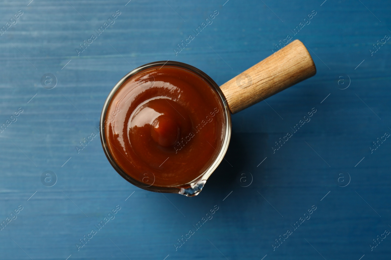 Photo of Tasty barbeque sauce on blue wooden table, top view