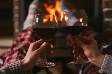 Couple with glasses of red wine near burning fireplace, closeup