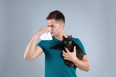 Young man with cat suffering from allergy on grey background