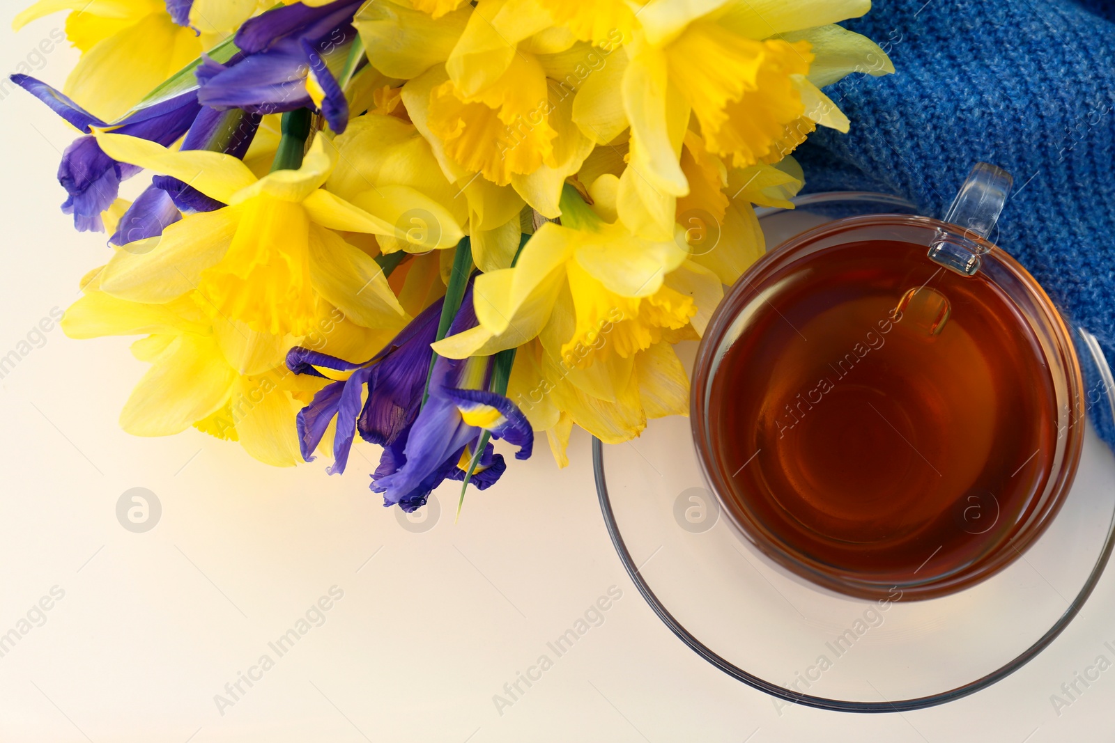 Photo of Cup of aromatic tea, beautiful yellow daffodil and iris flowers on white table, flat lay