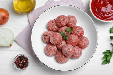 Many fresh raw meatballs and ingredients on white wooden table, flat lay