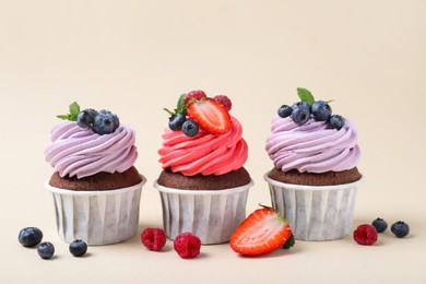 Photo of Different delicious cupcakes with cream and berries on beige background
