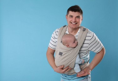 Photo of Father holding his child in sling (baby carrier) on light blue background. Space for text