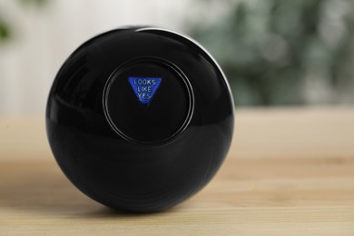 Magic eight ball with prediction Looks Like Yes on wooden table, closeup