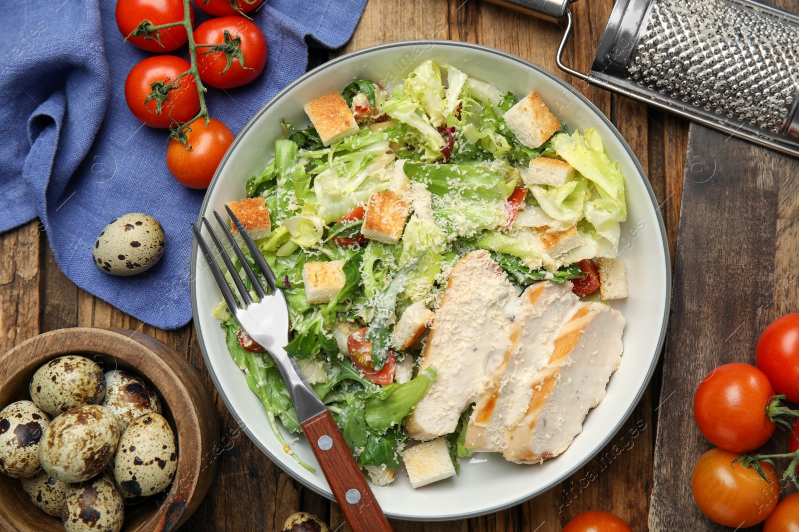 Photo of Delicious Caesar salad in bowl on wooden table, flat lay