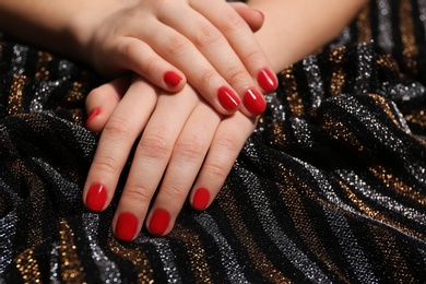 Woman with red manicure on sparkling dark fabric, closeup. Nail polish trends