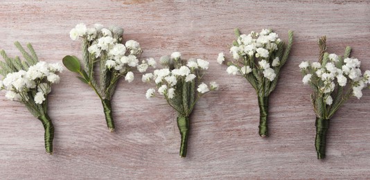 Many small stylish boutonnieres on light wooden table, flat lay