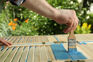 Photo of Man painting wooden surface with blue dye outdoors, closeup